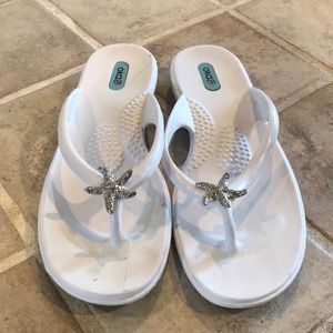 Oka B silver sea star decorated white flip flops.